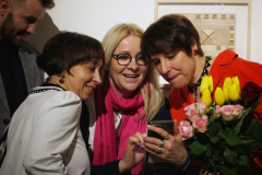 Joanna Imielska z przyjaciółkami ogląda coś w telefonie. Wszystkie się uśmiechają. Artystka trzyma bukiety kwiatów.