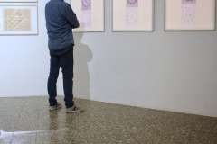 Samotny mężczyzna ubrany w dżinsy i niebieską koszulę ogląda prace wyeksponowane w rzędzie na jasnej ścianie.