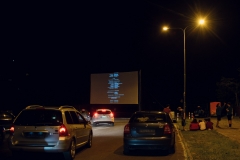 Ekran kina samochodowego widziany z miejsca parkingowego.  Lampa po prawej stronie oświetla zgromadzonych pod nią ludzi.