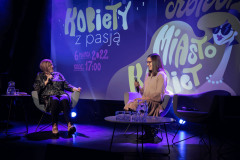 Na scenie siedzące w fotelach Anna Pilarska i Agnieszka Pilarska. Za nimi wyświetlony slajd Kobiety z pasją Konin Miasto Kobiet.
