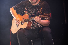 Marcin Żabiełowicz siedzi i gra na gitarze.