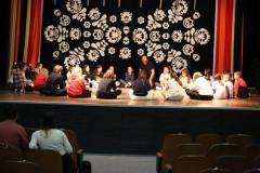 Na scenie tworząc koło siedzą po turecku dzieci w towarzystwie Jarosława Paczkowskiego. W tle kurtyna z ludowym motywem.