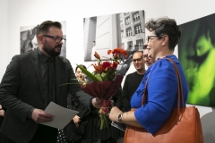Robert Kuciński wręcza Agnieszce Arasimowicz ozdobiony czerwoną bibułą bukiet kwiatów.