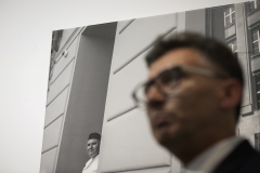 Rozmyta twarz Krzysztofa Pawlaka, dyrektora Państwowego Liceum Sztuk Plastycznych w Kościelcu. W tle wyrazista, czarno-biała fotografia zawieszona na białej ścianie. Przedstawia pulchnego mężczyznę w czarnej czapce wychylonego zza zewnętrznej ściany budynku.