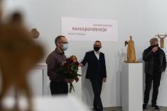 Od lewej: Stanisław Kośmiński z bukietem kwiatów, Robert Brzęcki opiera prawą rękę na postumencie i krzyżuje nogi, Antoni Grabowski prawą ręką sięga do maseczki na ustach, lewą trzyma w kieszeni spodni