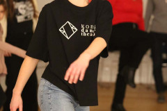 W centrum kadru dziewczyna w czarnej koszulce z logo Konińskiego Teatru Tańca i niebieskich dżinsach.
