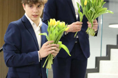 Dwóch chłopaków w garniturach stoi na stopniach schodów. W dłoniach trzymają bukiety żółtych tulipanów.