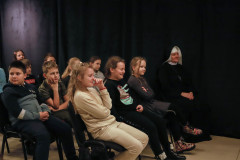 Zbliżenie na publiczność siedzącą przy ciemnej kotarze. W pierwszym rzędzie trzy dziewczynki i zakonnica.