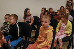 Zbliżenie na dzieci siedzące przy ścianie na ciemnych wyściełanych krzesłach.
