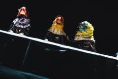 Zdjęcie ukośne. Trzy osoby za stołem z założonymi ptasimi głowami.