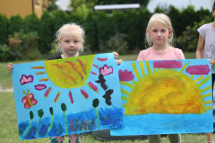 Dwie dziewczynki pozują do zdjęcia z pracami przedstawiającymi słońce.