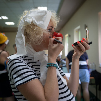 Paulina Pachulska-Wojdak sfotografowana z prawego profilu w pasiastej koszulce i nosem klowna. Robi makijaż.