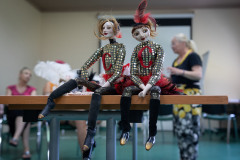 Dwie marionetki seidzące na brzegu stolika. Brokatowe bluzeczki z czerwoną literą C.