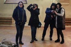 Cztery osoby z aparatami fotograficznymi. Ubrane w zimowe kurtki. Zdjęcie w starym pomieszczeniu z drewnianą podłogą.