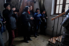 Grupa fotografów stoi przy drzwiach wejściowych wenątrz budynku. Pryz drzwiach wiszą kotary. Po prawej fragment drewnianych schodów z balustradą.