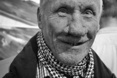 Zbliżenie na uśmiechniętego starszego mężczyznę. Pod szyją zawiązana arafatka. Zdjęcie czarno-białe.