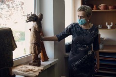 Krystyna Mikołajczak dłonią bada drewnianą rzeźbę mężczyzny, który na ramieniu niesie siano.
