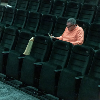 Rzędy pustych foteli w sali widoiwiskowej i aktor Krzysztof Majchrzak przeglądający kartki.