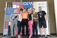 Na tle baneru OKFA stoją pracownicy CKiS w Koninie pozując do zdjęcia. Między nimi aktor Krzysztof Majchrzak.