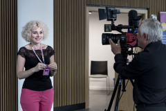 Paulina Pachulska-Wojdak stoi przed kamerą i z uśmiechem prezentuje identyfikator OKFA.