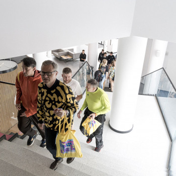 Zdjęcie z góry. Czterej mężczyźni wchodzą po schodach. Za nimi białe filary i publiczność idąca ich śladem.