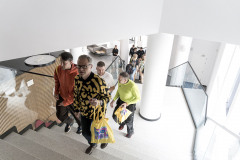 Zdjęcie z góry. Czterej mężczyźni wchodzą po schodach. Za nimi białe filary i publiczność idąca ich śladem.