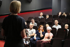 Monika Kuczyniecka zwrócona plecami do obiektywu, przemawia do widzów zasiadających w fotelach.