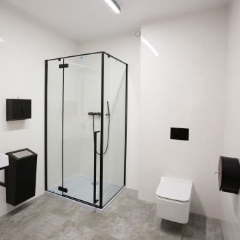 Łazienka w garderobie. Po lewej umywalka i lustro. Obok prysznic i sedes. Wnętrze utrzymane w bieli z czarnymi akcentami.