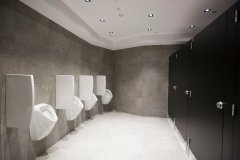 Rząd białych pisuarów naprzeciwko rzędu czarnych kabin toaletowych