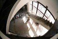 Zdjęcie zrobione z góry. Widać filar i pozostałości schodów. Podłoga pokryta gruzem i pyłem budowlanym.