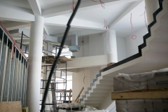 Hol główny. Z białego sufitu zwisają czerwone kable. Widać fragment schodów i rusztowanie.