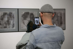 Widziany z tyłu mężczyzna w szarej wełnianej czapce i dżinsowej bluzie robi zdjęcie telefonem komórkowym.