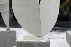 Aluminiowa rzeźba Wacława Staweckiego. Przedstawia zagięte koło z wyciętym niewielkich rozmiarów trójkątem w górnej części.