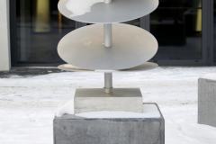 Rzeźba Donata Szulińskiego. Cztery aluminiowe dyski nabite jeden po drugim na pionowy słup. Podstawą dzieła jest kamienny graniastosłup.