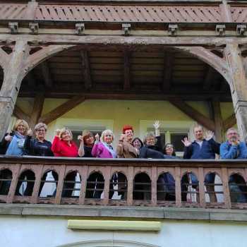 Uczestnicy pleneru na drewnianym balkonie pozują do zdjęcia. Zdjęcie robione z dołu.