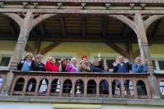 Uczestnicy pleneru na drewnianym balkonie pozują do zdjęcia. Zdjęcie robione z dołu.