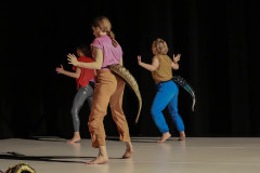 Na scenie zwrócone plecami do obiektywu trzy kobiety w układzie tanecznym. W pasie mają przypięte przypominające ogony macki.