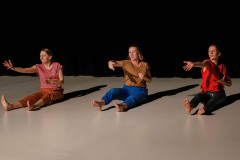 Fragment spektaklu. Trzy kobiety siedzą na scenie z wyciągniętymi przed siebie nogami. Wyciągają przed siebie prawe dłonie.