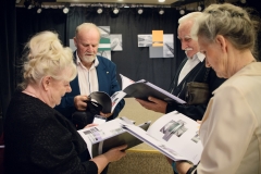Cztery osoby odwrócone ku sobie twarzami oglądają katalogi poświęcone wystawie poplenerowej Kołobrzeg 2019