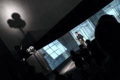 Zdjęcie robione z ukosa. Aktor przed dekoracjami przedstawiającymi drzwi. Na pierwszym palnie ciemne sylwetki publiczności. W tle ściana Oskardu z cieniem reflektora.
