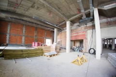 Sala klubowa w budowie. Ściany z cegły, betonowy strop i trzy białe filary. Na podłodze sterta desek, palety i zwoje kabli.