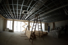 Metalowa konstrukcja sufitu sali w-f. Pośrodku drabina i deski. Po prawej dwóch robotników.