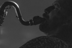 Widziany z lewego profilu Piotr Mełech gra na saksfonie. Zdjęcie czarno-białe.