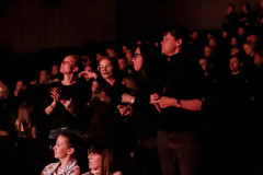 Publiczność w trakcie koncertu. W centrum kadru stoją cztery kobiety w czerni.