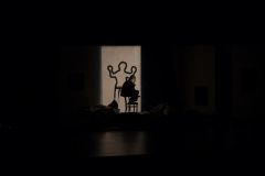 Mrok. Oświetlony jedynie pionowy prostokąt z obrysowaną ludzką sylwetką. Na krześle siedzi aktor.