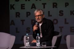 Tomasz Rodowicz, dyrektor Teatru Chorea zasiad w sszarym fotelu. W prawej ręce trzyma mikrofon. Przed nim na stoliku szklanka i dwie butelki wody mineralnej.