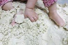 Zbliżenie na dziecięce stopy i dłonie zanurzone w piasku.