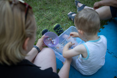 Widok z góry na kobietę i dziecko siedzące na macie. Dziecko trzyma pudełko z wodą, w którym pływają kolorowe kamyki.