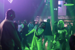 Uczestnicy silent disco podczas tańca. W tle bar z butelkami. Zielone światła reflektorów.