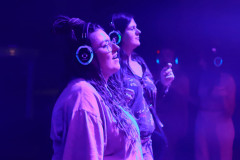 Dwie kobiety sfotografowane z prawego profilu. Na uszach słuchawki. Jedna z nich śpiewa.